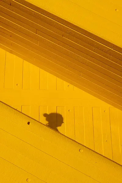 Profil féminin en ombre portée sur une architecture jaune moderne : comme la traductrice professionnelle, une présence essentielle mais souvent invisible.